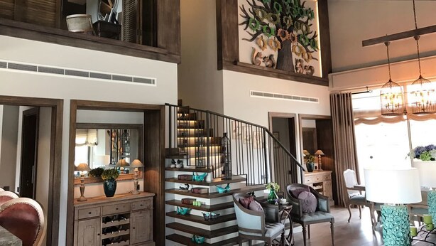 A spacious living area with a staircase, a large tree mural, and a dining area with a chandelier. - Regnum Golf Country 3 bedroom 4 (Bodrum)
