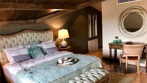 A bedroom with a large bed, a bedside table with a lamp, a bench, a chair, and a round mirror on the wall. - Regnum Golf Country 3 bedroom 4 (Bodrum)