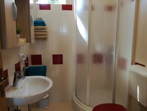 Une salle de bain avec un lavabo blanc, une douche en verre et des toilettes.