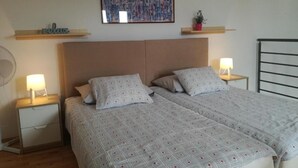 A bedroom with two beds, a headboard, bedside lamps, a wall-mounted artwork, and a shelf with decorative items. - Apartments Henc (Novigrad)