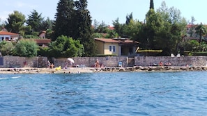 Une zone côtière avec un mur de pierres, des chaises de plage et des gens qui se détendent au bord de l’eau.