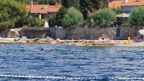 Une zone côtière avec un mur de pierre, une plage et des bâtiments aux toits recouverts de tuiles rouges.