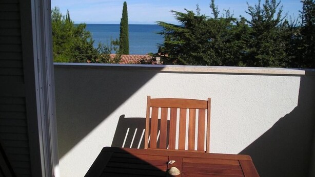 A balcony with a wooden table and chair, overlooking a body of water and greenery. - Apartments Henc (Novigrad)