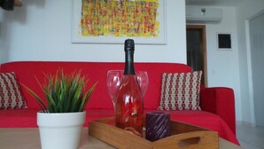 A red sofa with patterned cushions, a potted plant, a bottle of red liquid, and two glasses on a wooden tray. - Apartments Henc (Novigrad)