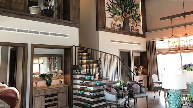 A spacious living area with a staircase, a large tree mural, and a dining area with a chandelier.