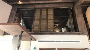 A modern interior with exposed wooden beams, a large window with blinds, and a ceiling fan.