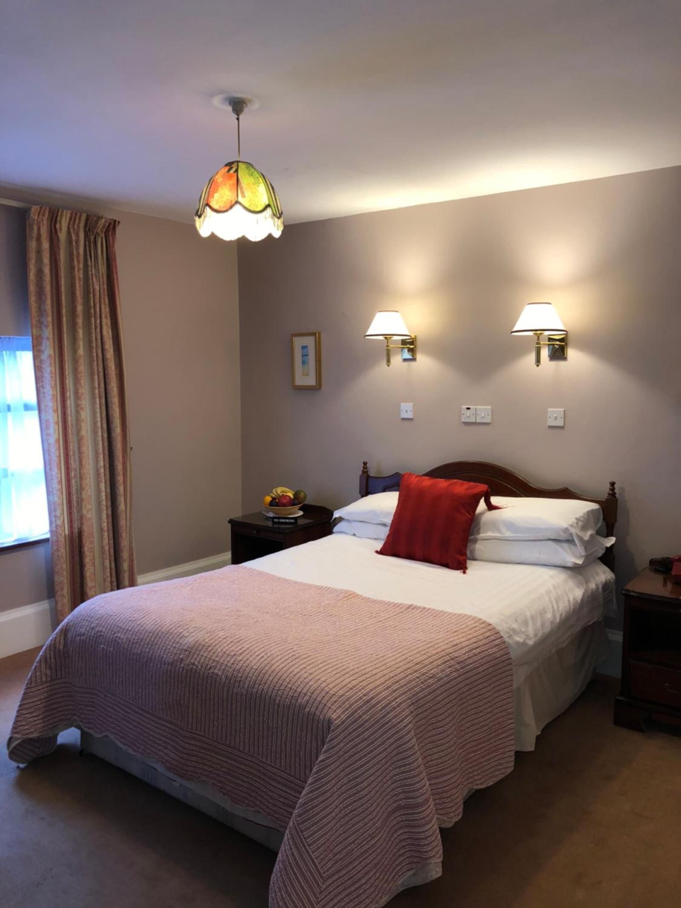 Una cama bien hecha con una colcha a rayas, dos lámparas de pared y un colgador de luz.