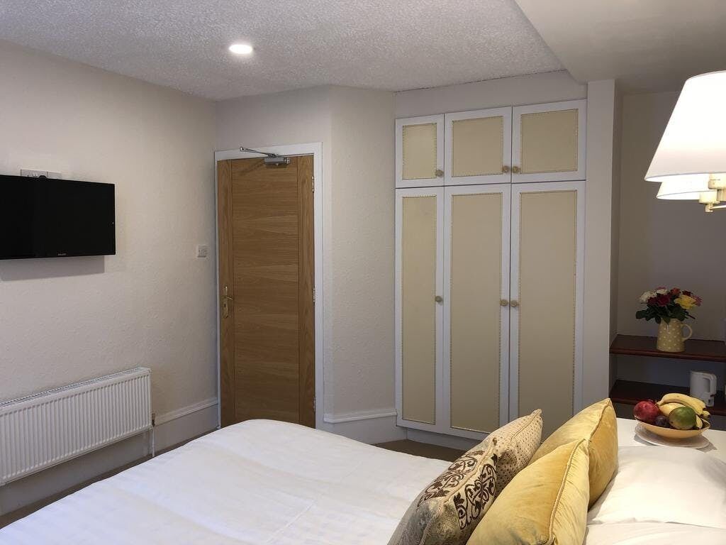 Un dormitorio con cama, armario, televisor y mesita de noche con lámpara y frutero.