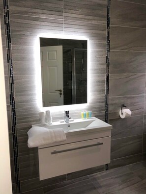 A modern bathroom with a large mirror, a sink, and a shower.