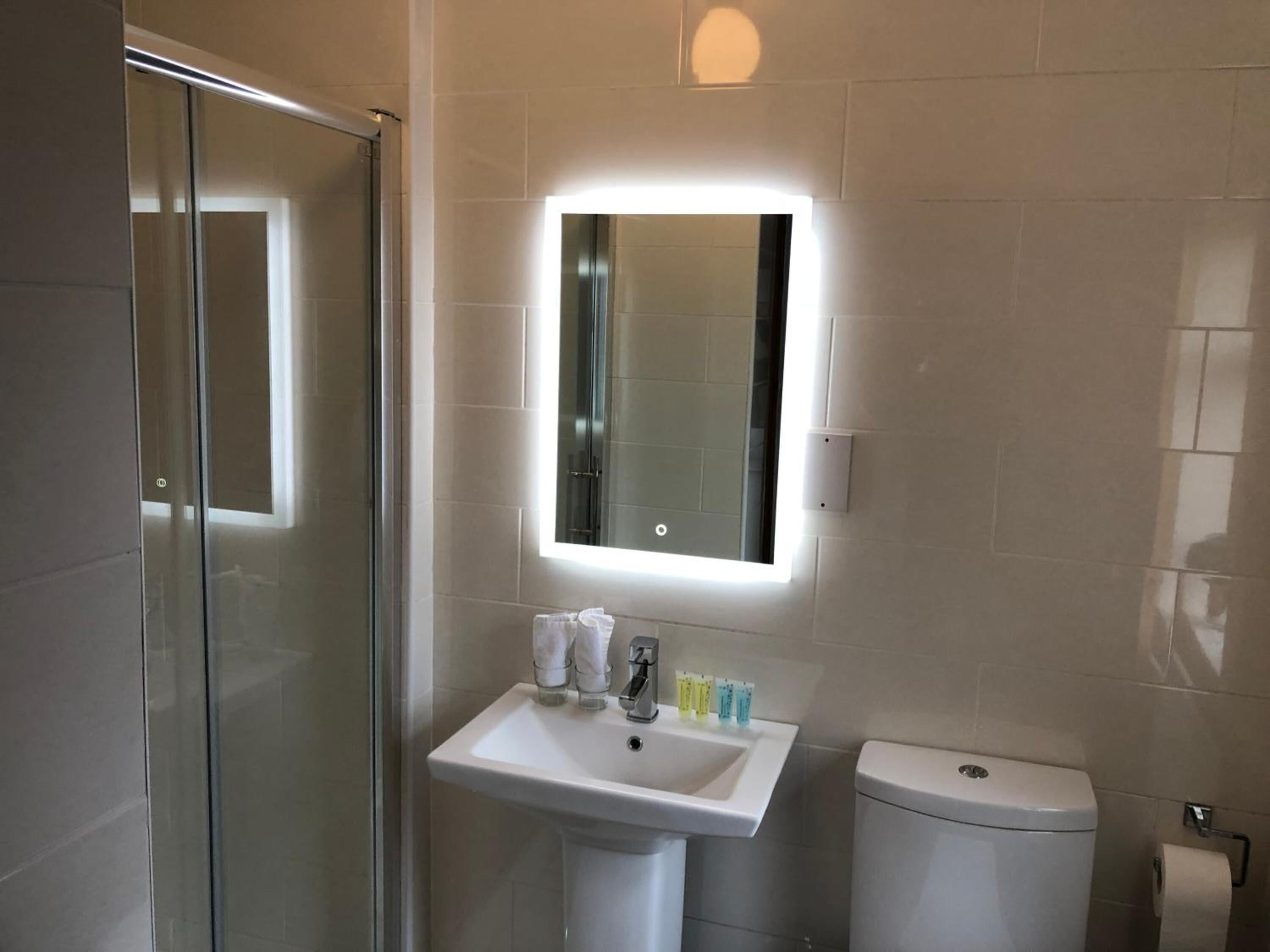 Un baño moderno con cabina de ducha de vidrio, un lavamanos blanco con espejo y un inodoro.