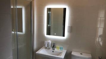 Un baño moderno con cabina de ducha de vidrio, un lavamanos blanco con espejo y un inodoro.