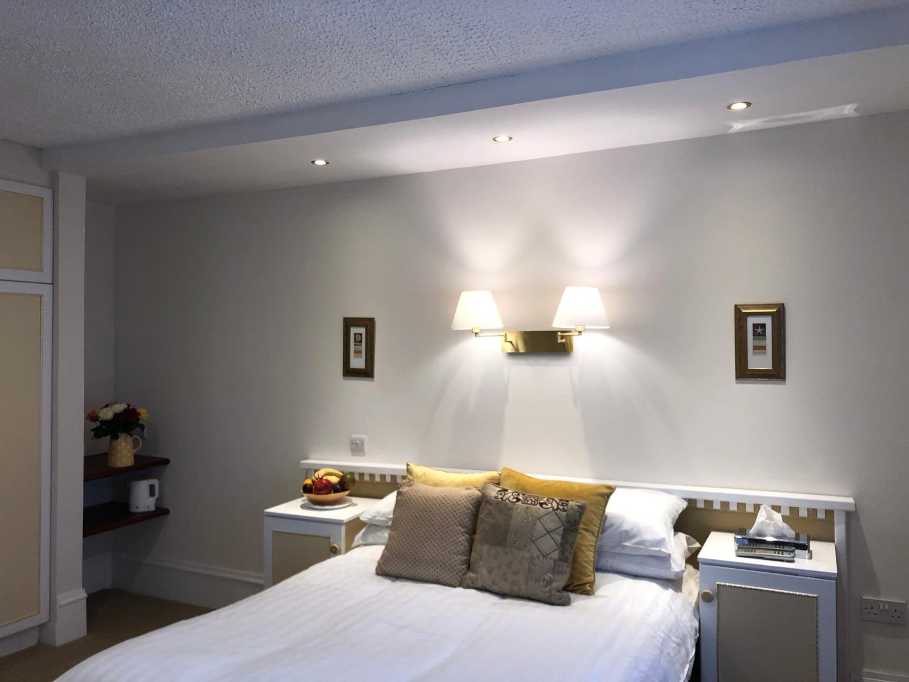 Un dormitorio ordenado con cama, mesitas de noche y lámparas de pared.