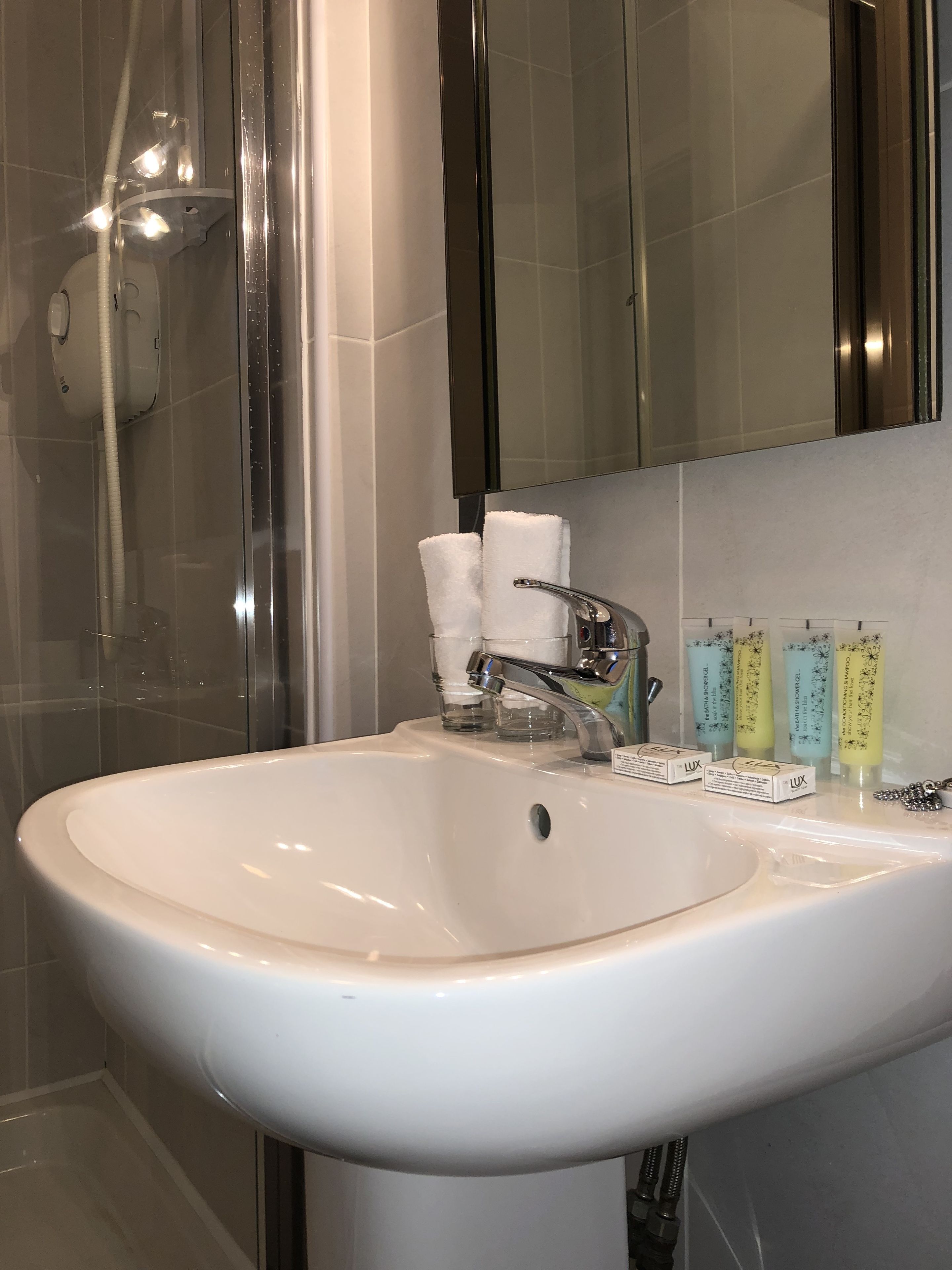 Een badkamer met een witte wastafel, een douchecabine van glas en toiletartikelen op de wastafel.