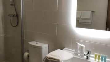 A bathroom with a toilet, shower, sink, and mirror.