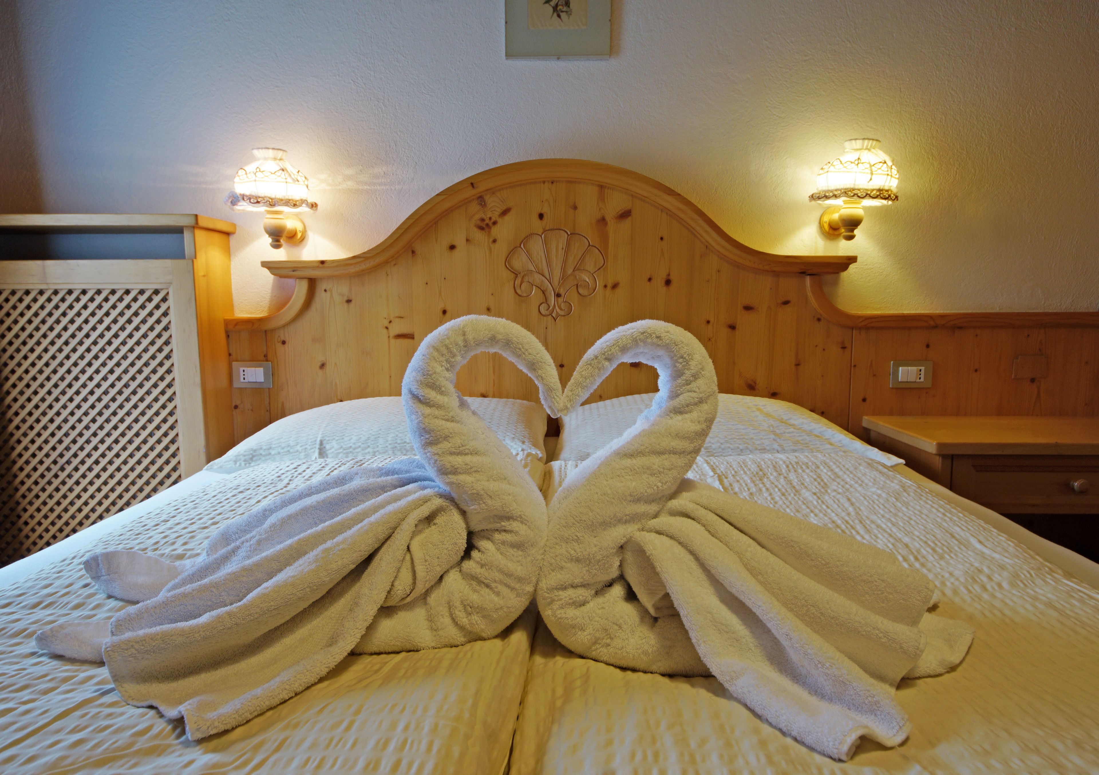 A bed with two towels arranged in a heart shape.