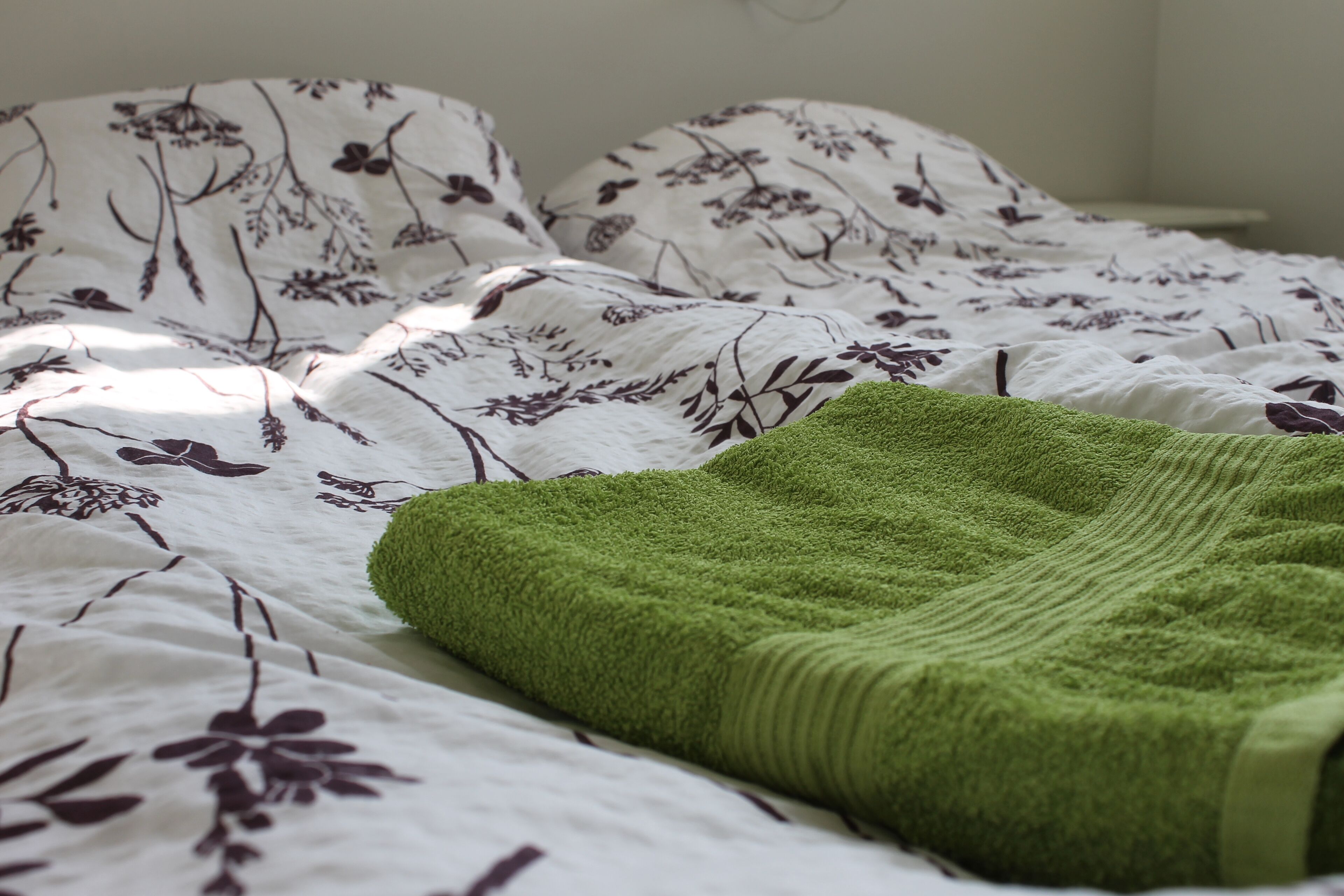Una cama con ropa de cama de estampado floral y una manta verde.