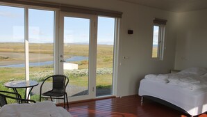 Un dormitorio con una cama, una silla, una mesita y vistas a un paisaje a través de amplias puertas correderas.