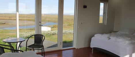 A bedroom with a bed, a chair, a small table, and a view of a landscape through large sliding doors.