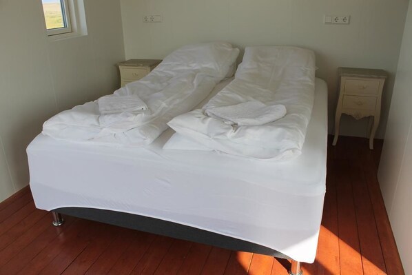 A single bed with white bedding in a room with wooden flooring and two bedside tables.