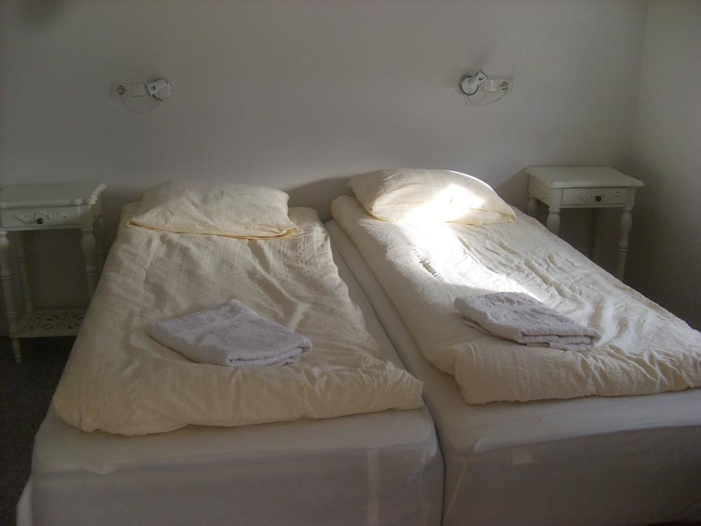 Deux lits simples avec du linge de lit et des oreillers blancs, une petite table de chevet à côté de chaque lit et une prise électrique au-dessus de chaque lit.