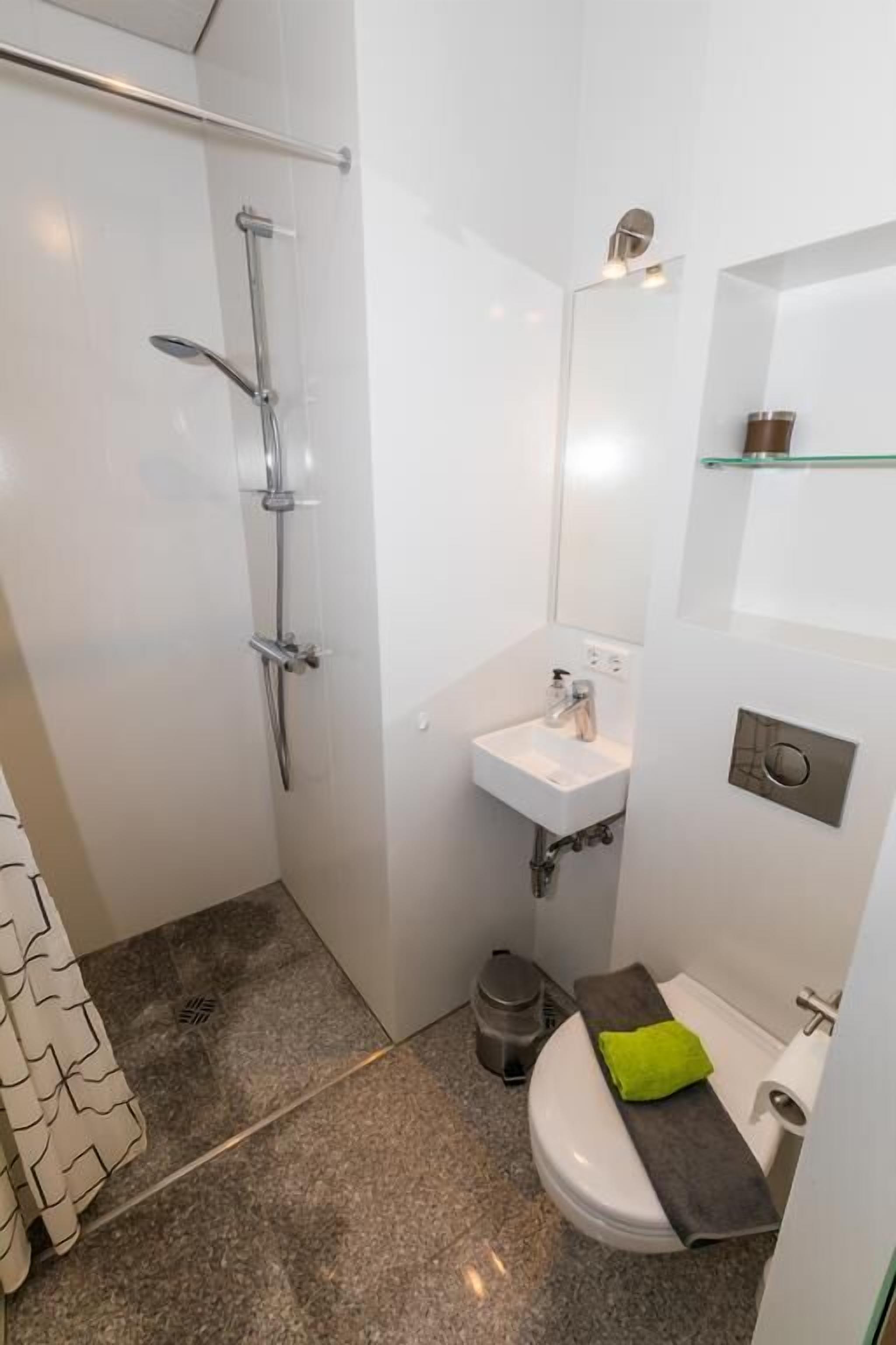 A compact bathroom with a shower, sink, toilet, and a small mirror.