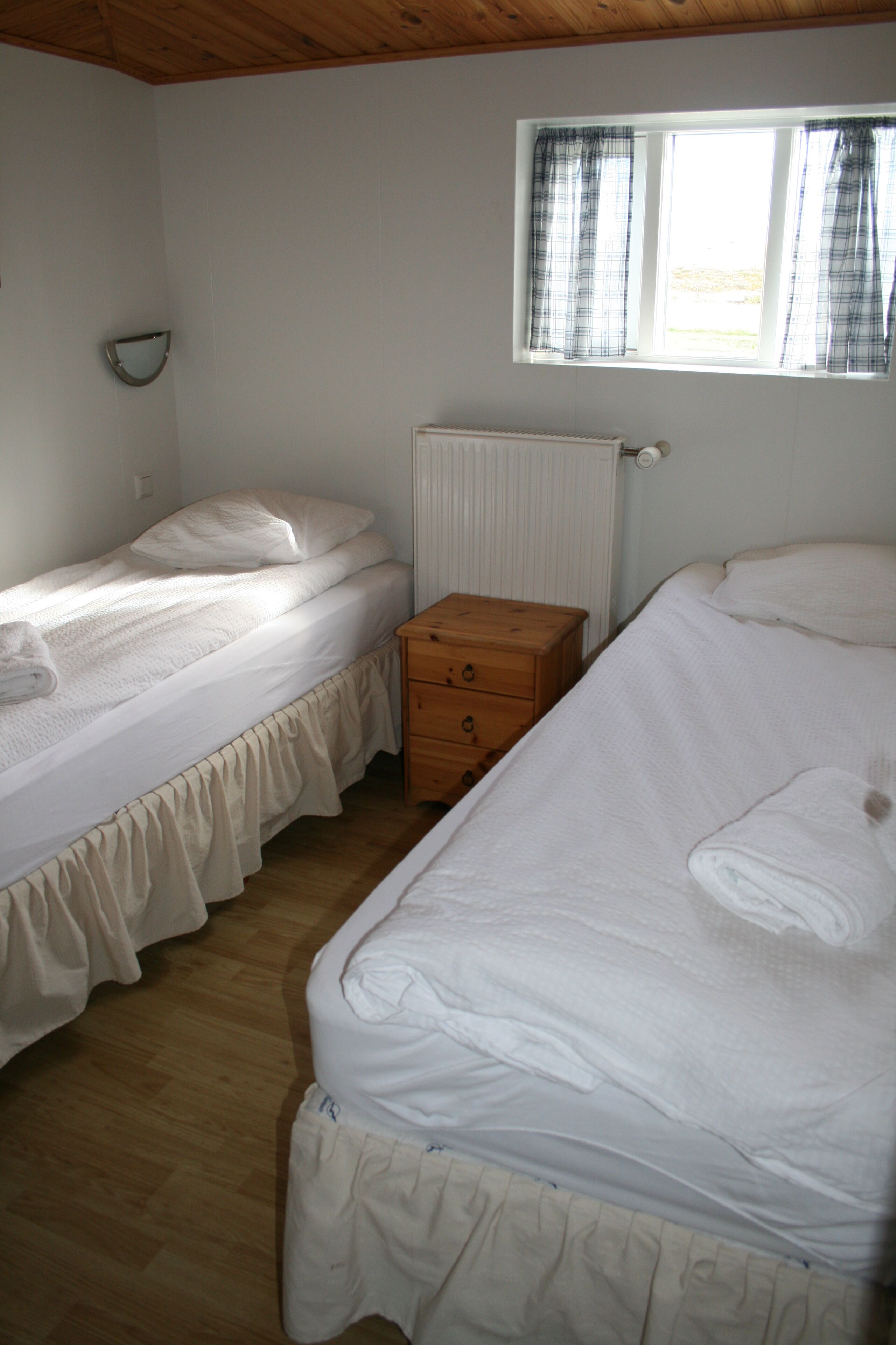 A bedroom with two beds, a wooden dresser, and a window with curtains.