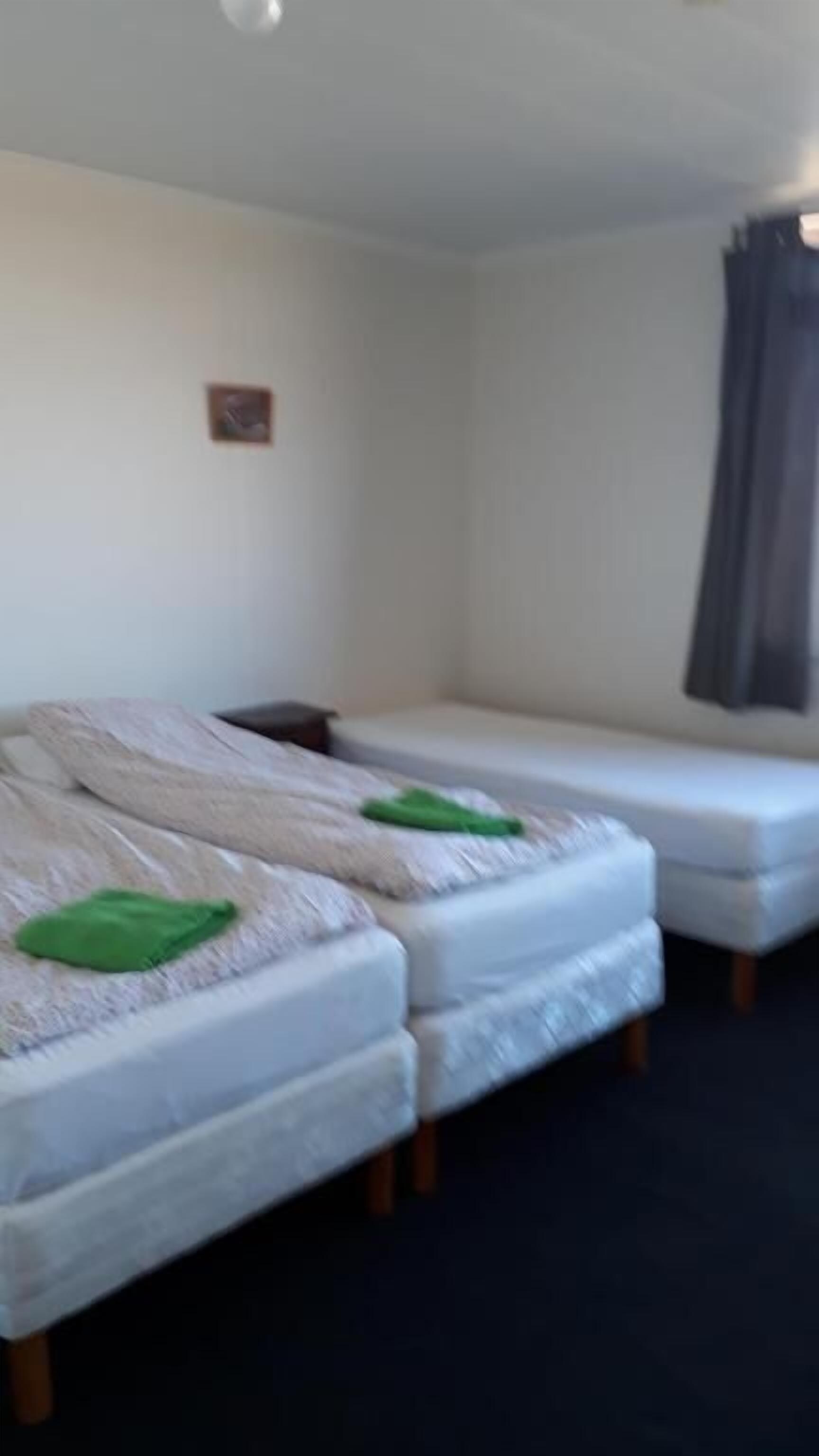 Quarto com duas camas, uma mesinha e uma janela com cortinas.