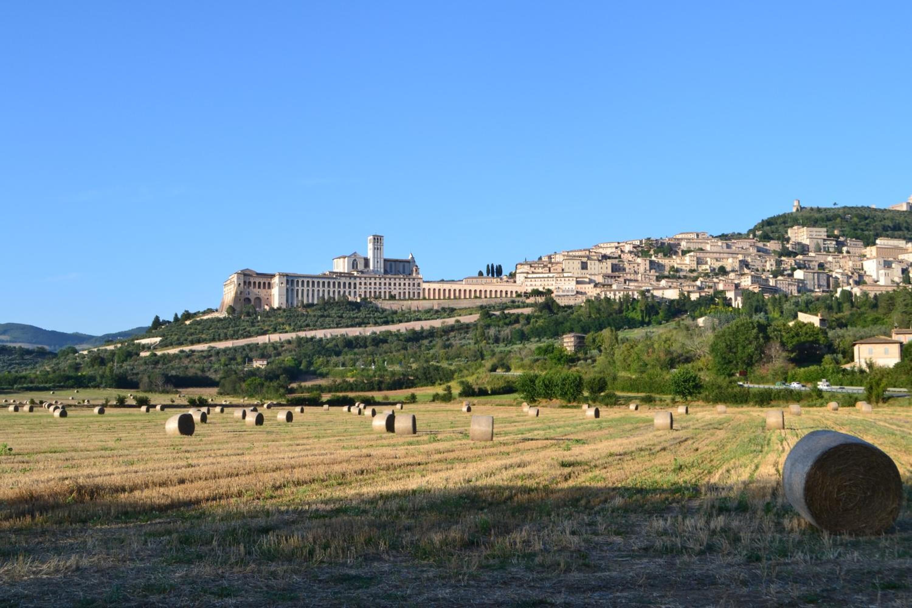 Paisaje rural con pacas de heno en un campo, un edificio grande con torre y un asentamiento en la ladera.