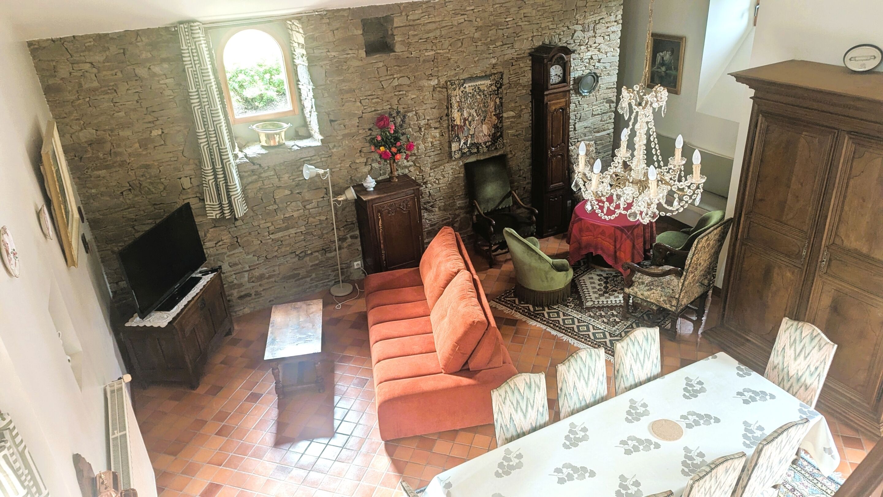 Quarto com paredes de pedra, um sofá, uma mesa, um candelabro e uma lareira.