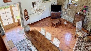 Un vaste espace de vie comprenant une table à manger en bois, un lustre, un téléviseur et un mur en pierre.