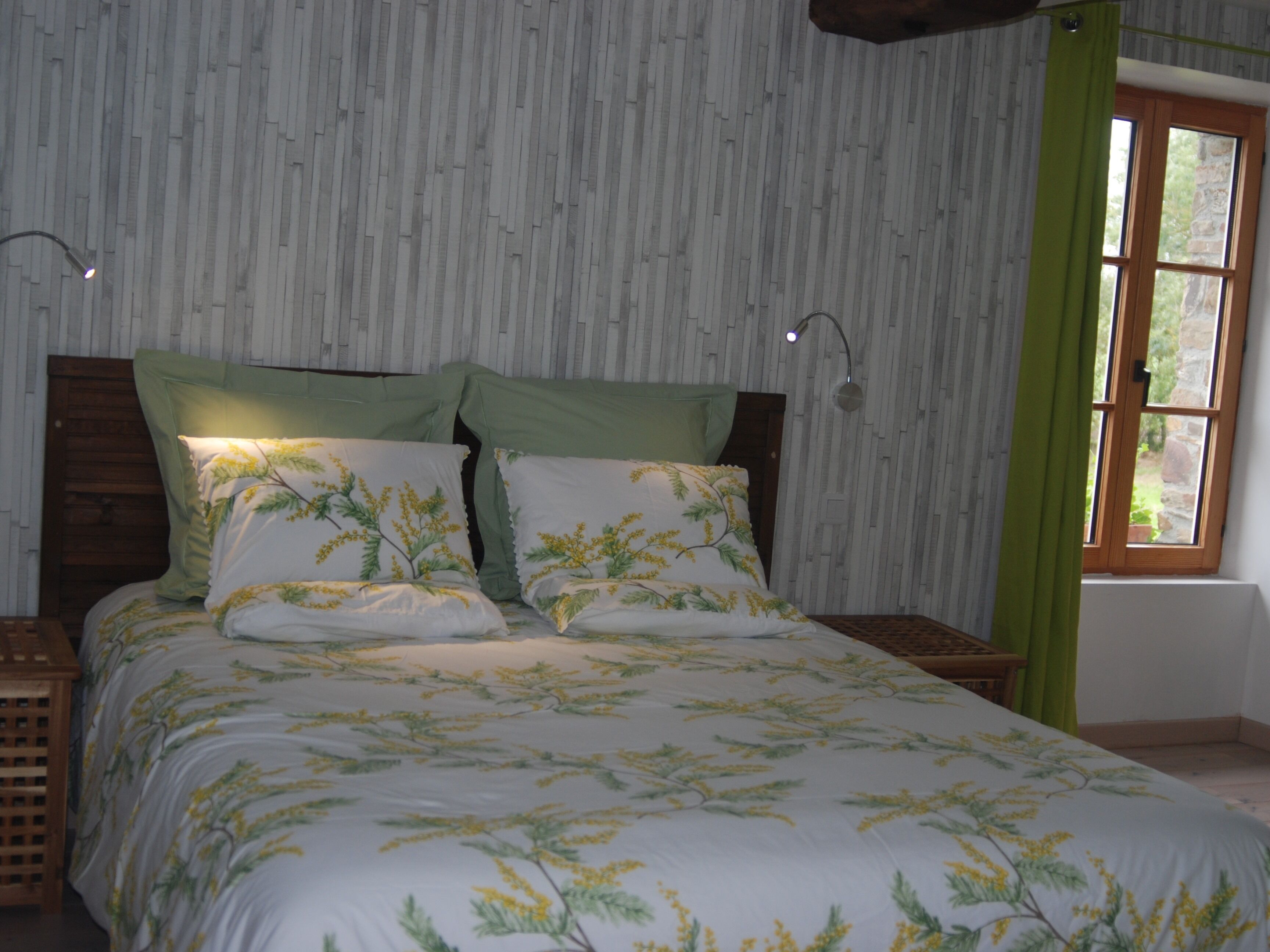 A bedroom with a bed, two bedside tables, a window with curtains, and a wall with a vertical pattern.