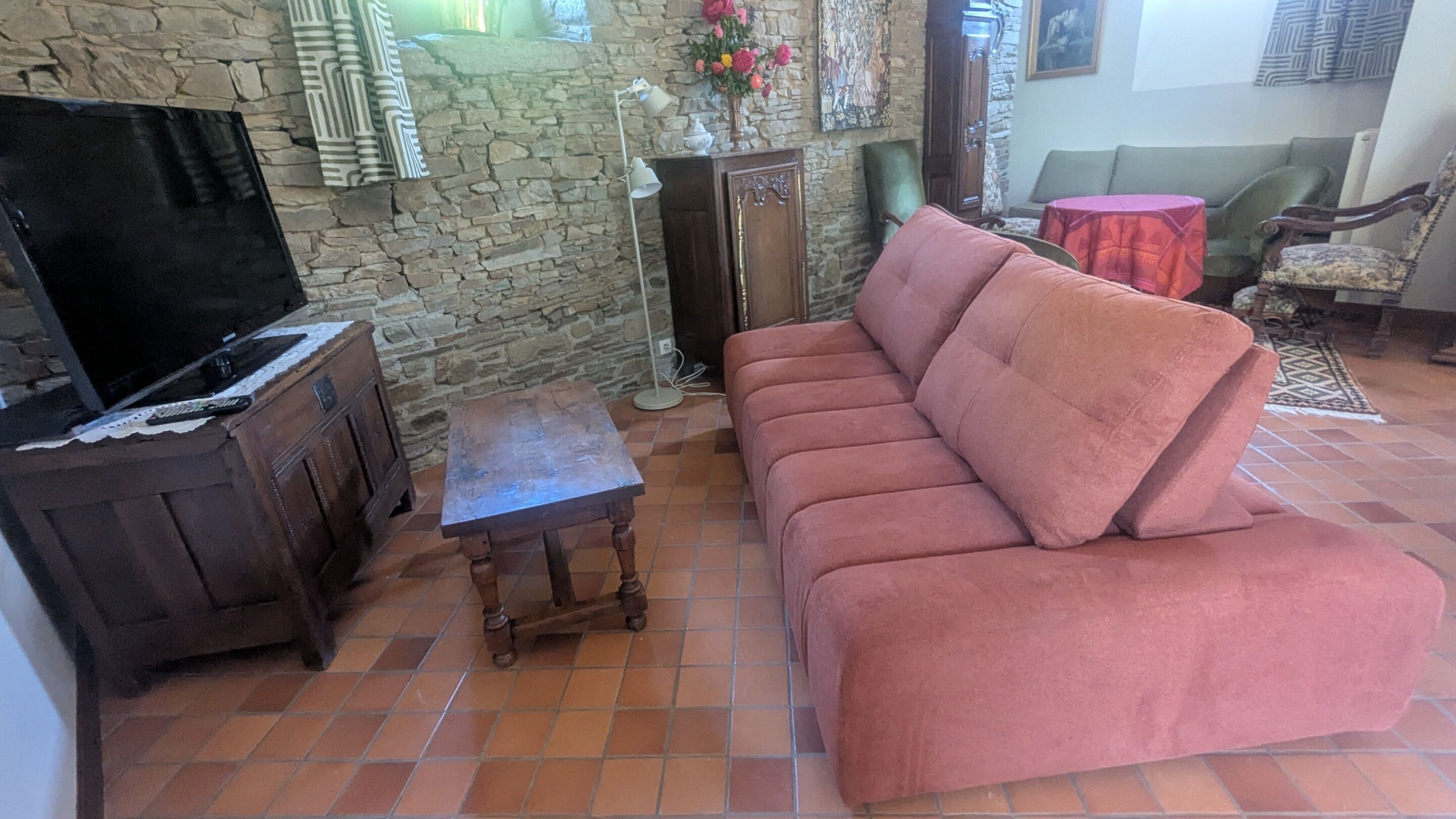 Un salon avec un canapé, un téléviseur posé sur un meuble, une petite table et un mur en pierre.