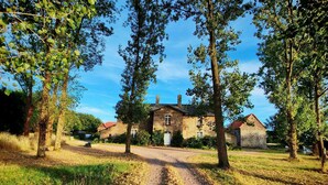 Un bâtiment en pierre avec un toit rouge, entouré d’arbres et bordé d’un chemin de gravier.