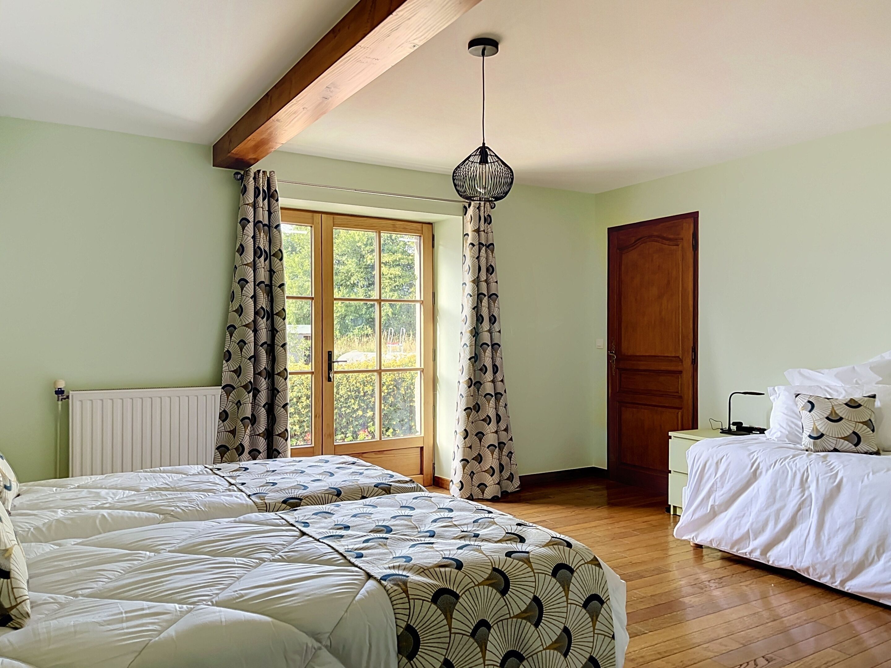 Una habitación con dos camas, una ventana con cortinas, una viga de techo de madera y una puerta.