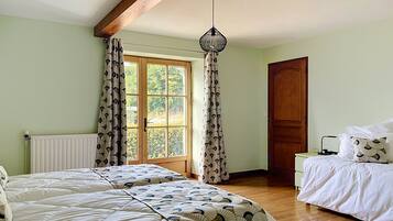 Una habitación con dos camas, una ventana con cortinas, una viga de techo de madera y una puerta.
