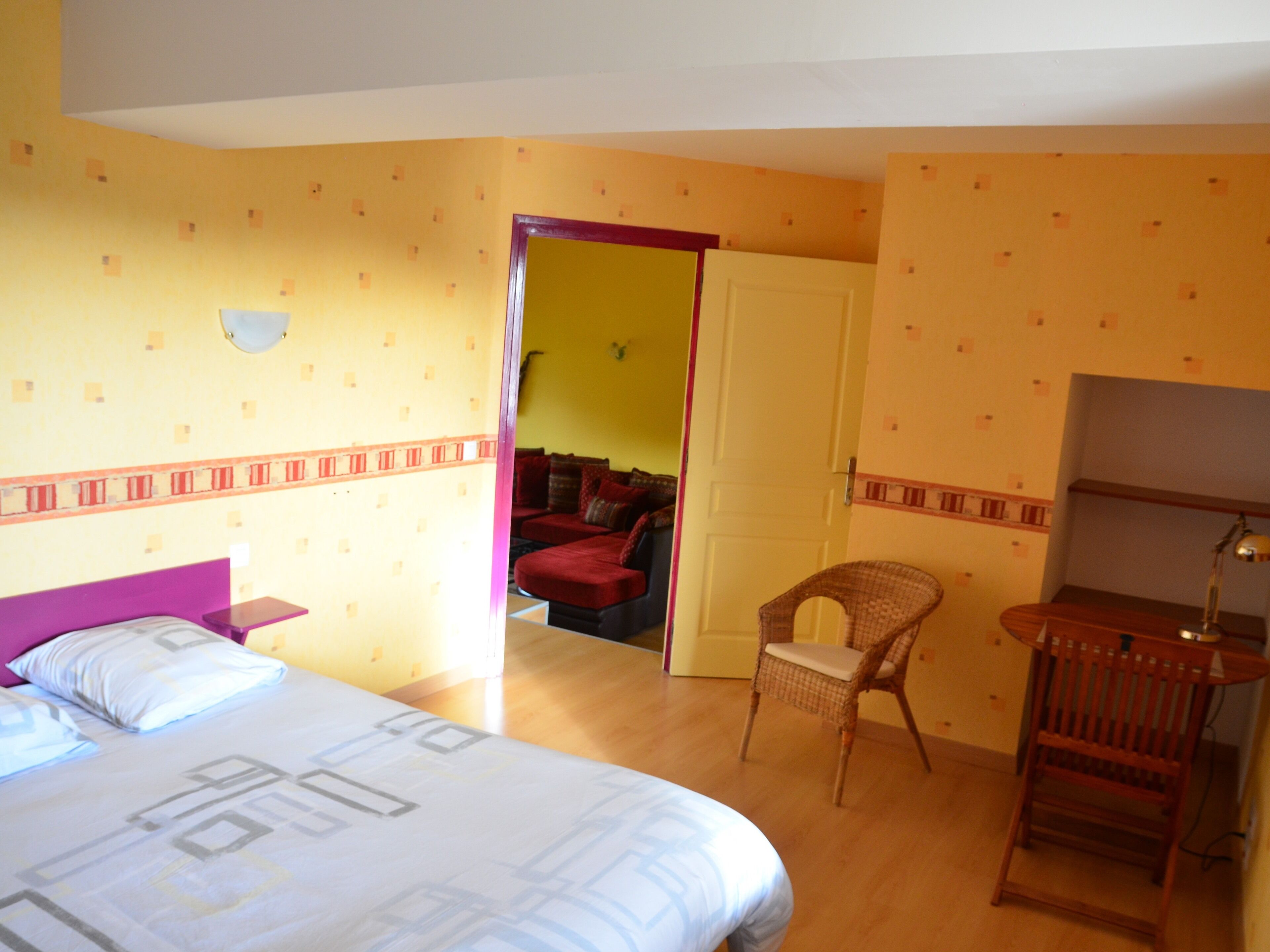 Una habitación de hotel con una cama, una silla, un escritorio y una puerta que da a otra estancia.