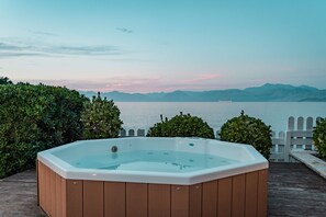 Relax in a hot tub on a deck overlooking a serene body of water and distant mountains.