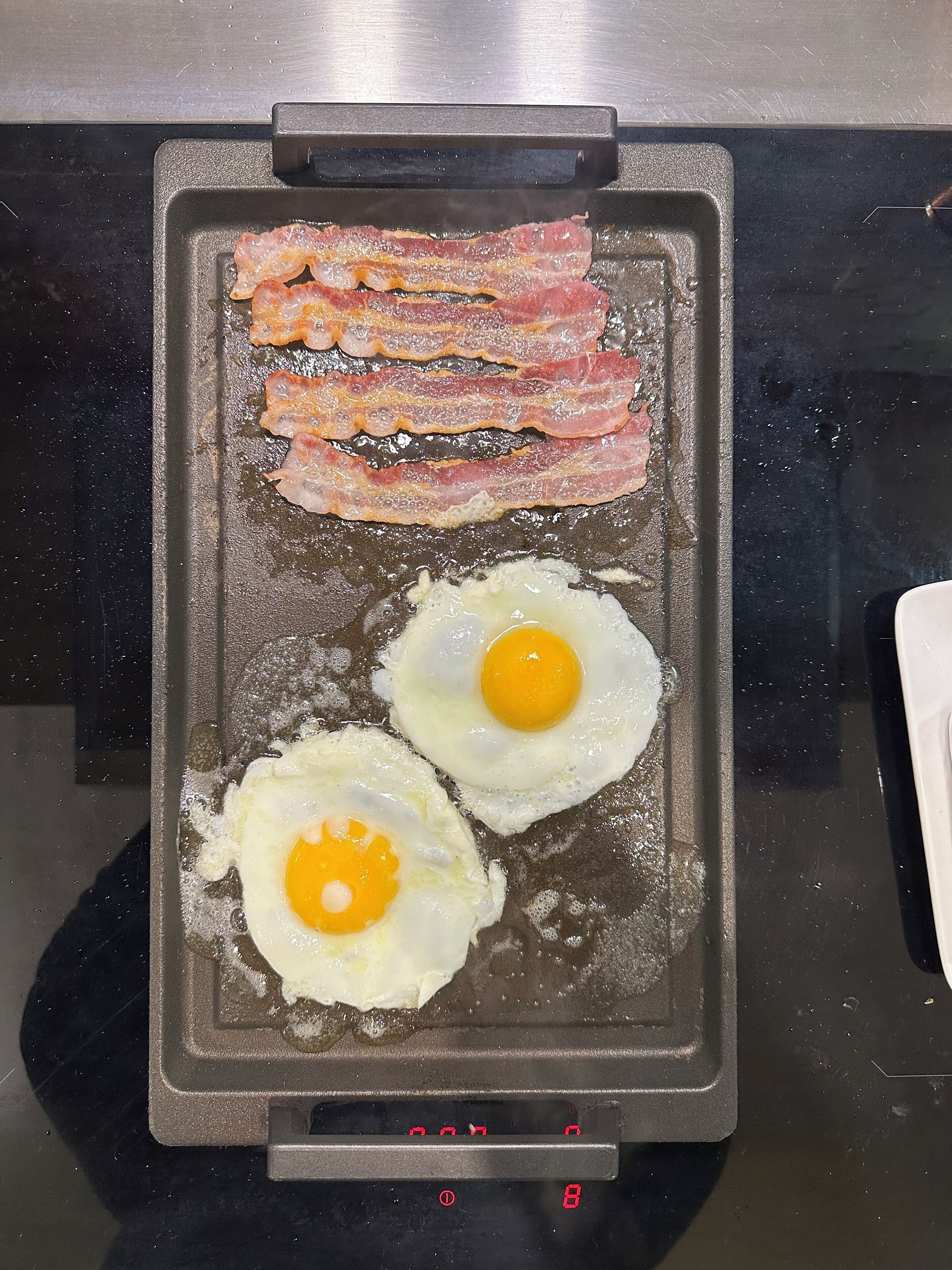 Ein Grillrost mit gebratenen Speckstreifen und zwei Spiegeleiern.