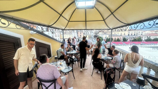 An outdoor dining area with tables and chairs under a canopy, overlooking a river and buildings. - B&B Sei Stelle (Sulmona)