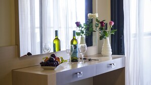 Habitació d'hotel amb un mirall gran, una tocador amb un bol de fruita, copes de vi i un vas amb flors.