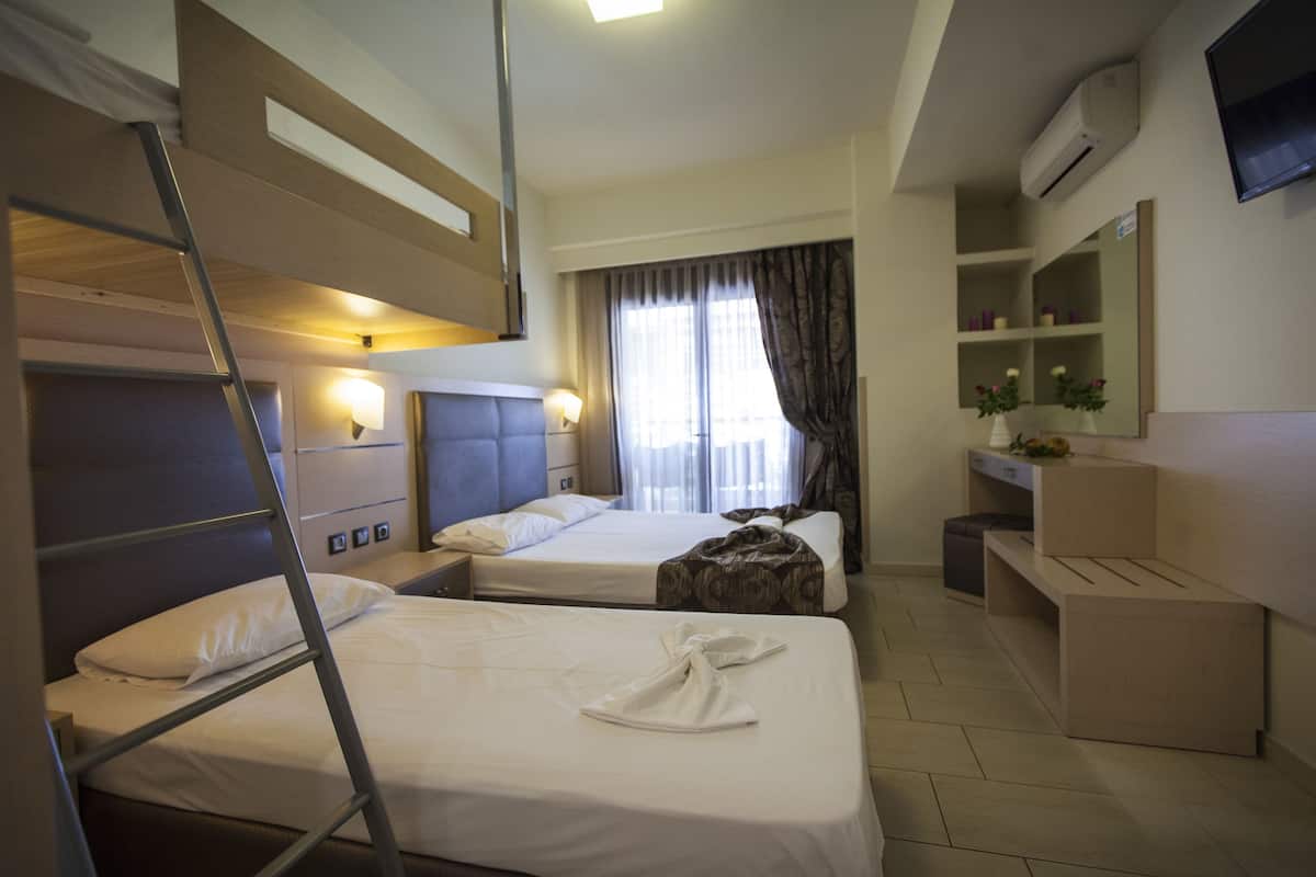 A hotel room with bunk beds, a desk, a chair, a TV, and a window with curtains.