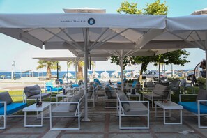 Terrasse extérieure avec parasols, vue sur la mer et café appelé « Amalthea Mare Cafe ».