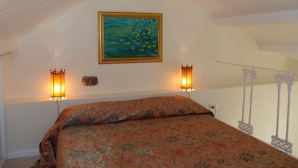 A bedroom with a sloped ceiling, a floral bedspread, a framed painting, and two wall-mounted lamps. - La casa di Ida (Locri)