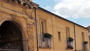 A building with a stone archway, a balcony with plants, and a window. - La casa di Ida (Locri)