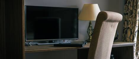 Una habitación de hotel con un televisor sobre un soporte, una lámpara y una cortina estampada.