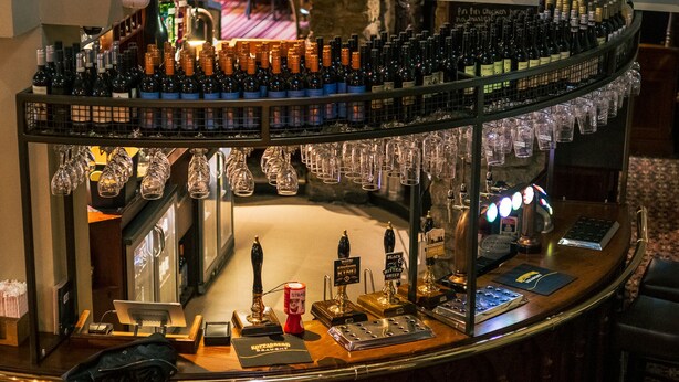 A bar area with multiple shelves of bottles and glasses, a cash register, and a computer. - The Old Mill (Durham)