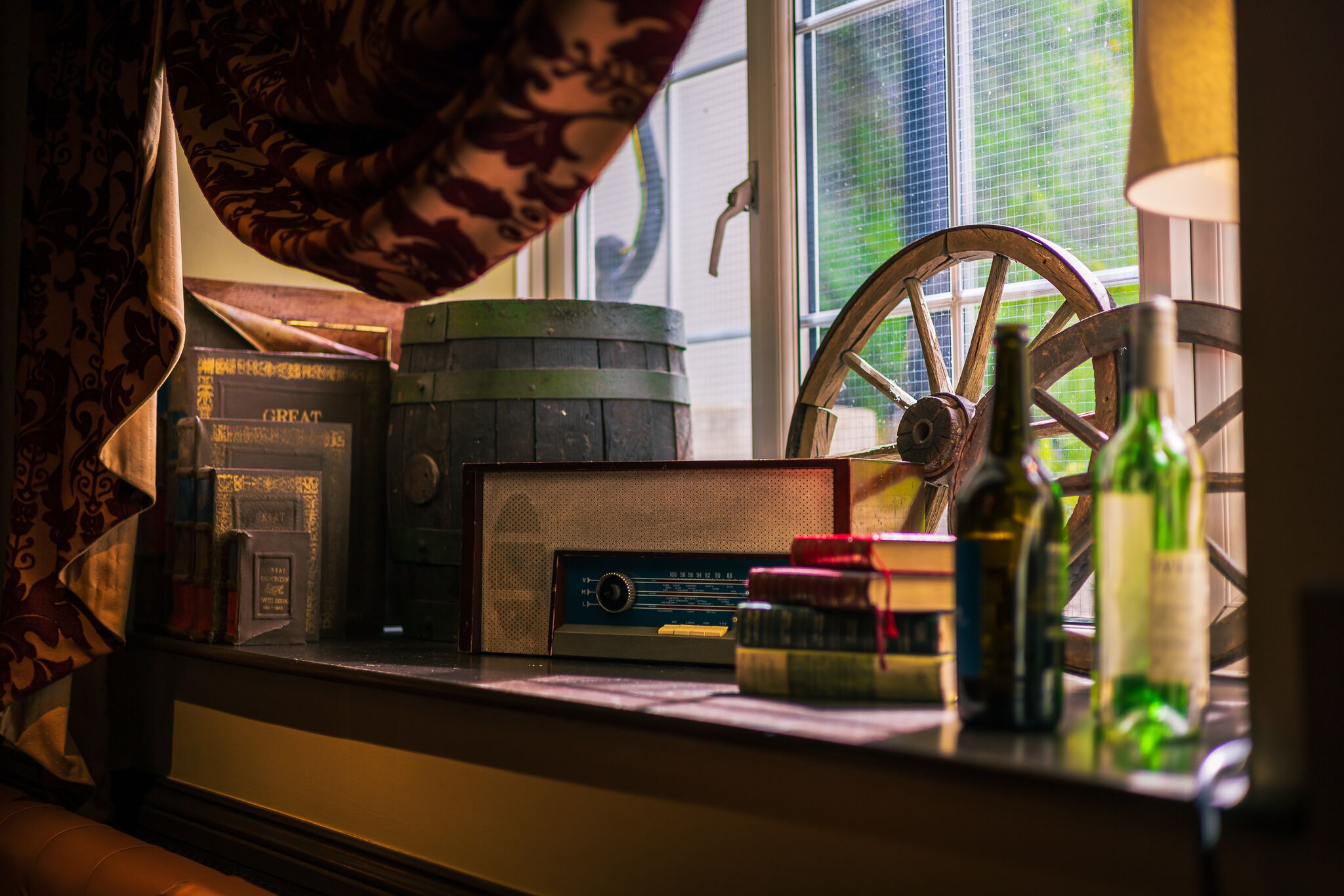 Een oude radio, boeken, een houten vat en flessen op een vensterbank.