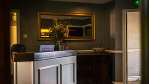 A reception desk with a mirror above it, a vase with flowers, and a laptop on the counter. - The Old Mill (Durham)