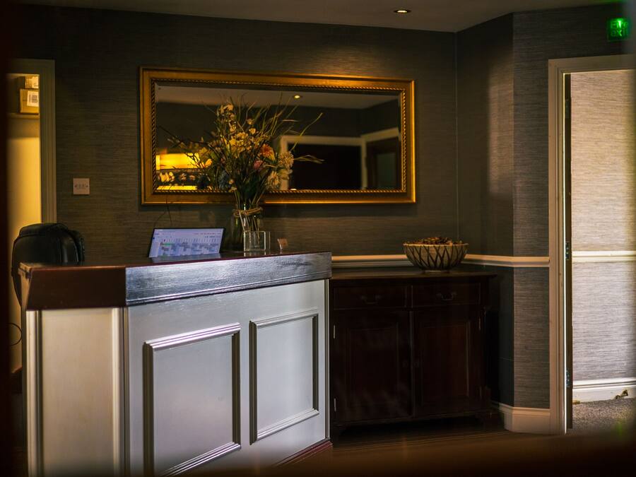 A reception desk with a mirror above it, a vase with flowers, and a laptop on the counter.