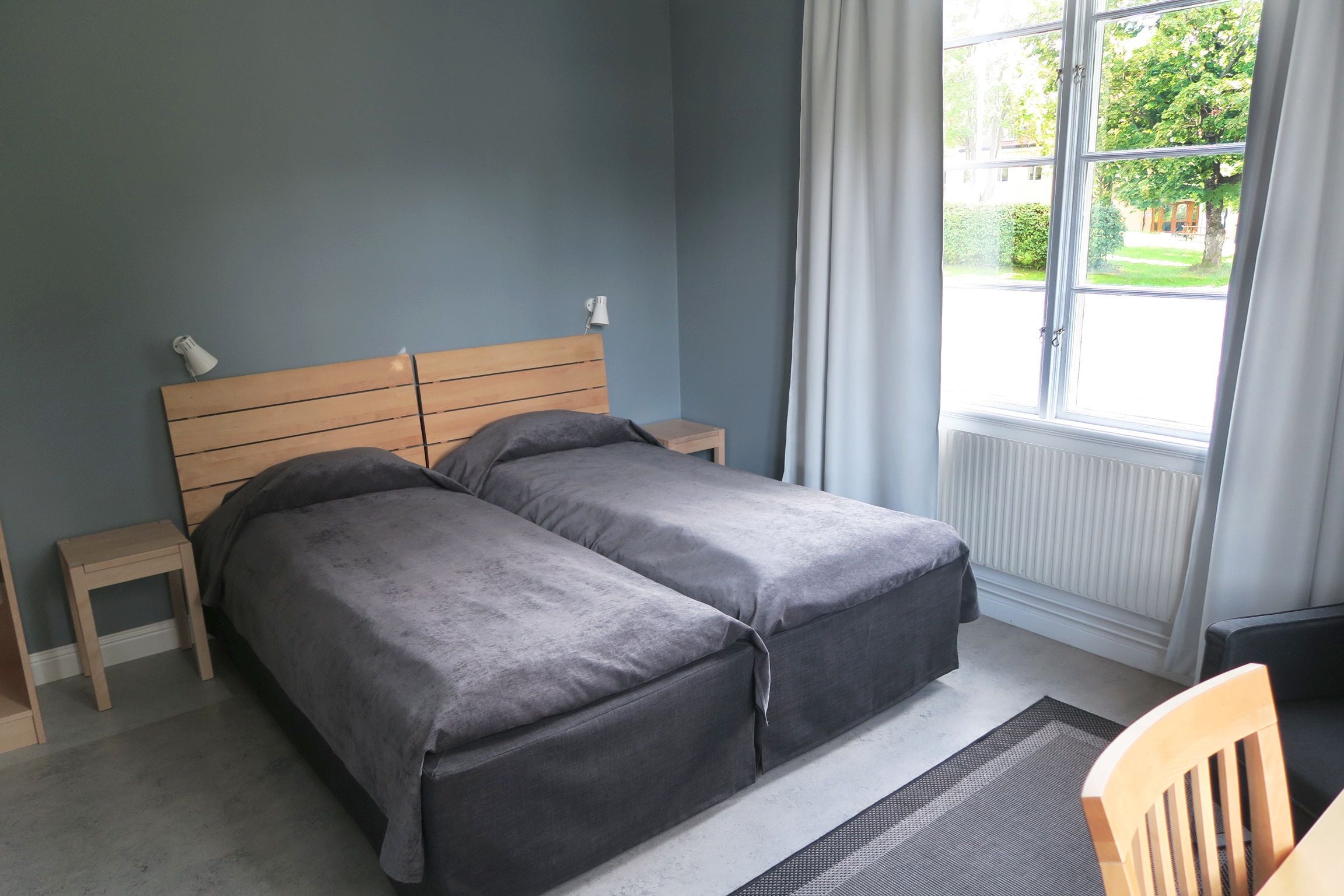 Een slaapkamer met een tweepersoonsbed, een nachtkastje, een stoel en een raam met gordijnen.